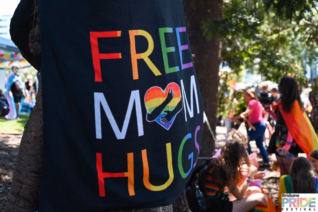 Close-up of a black t-shirt reading Free Mom Hugs in rainbow lettering, with the Fair Day crowd behind.